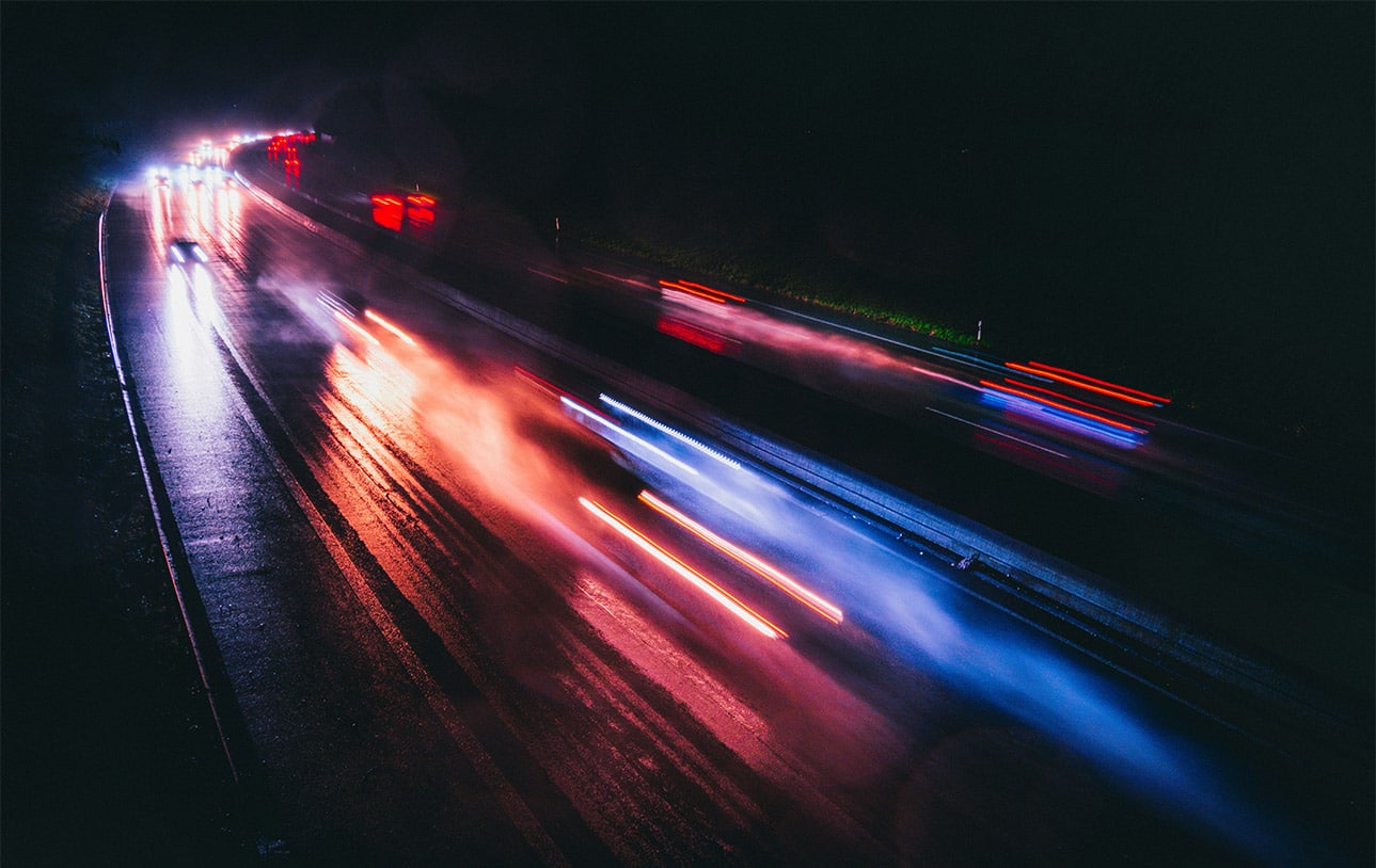 Blurred nighttime traffic on a wet roadway representing crash risk research